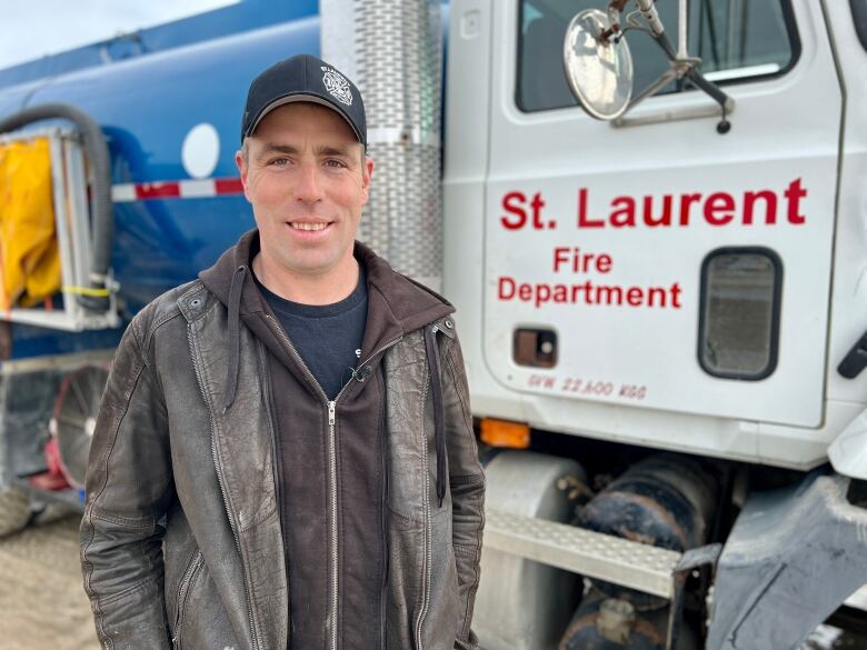 A man in a baseball cap stands in front of a pumper truck.