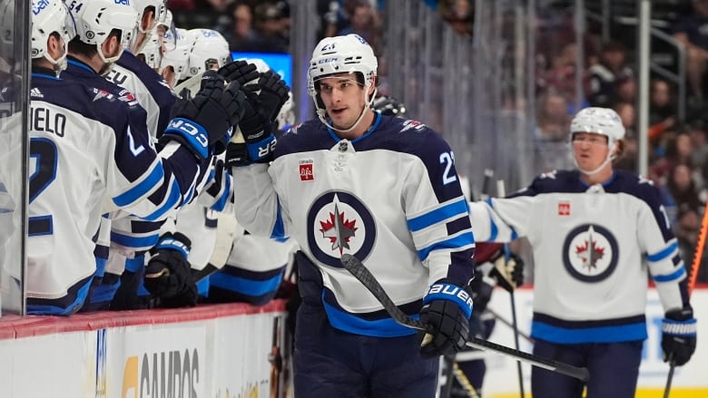 A Winnipeg Jets player high-fives teammates as he skates past the bench.