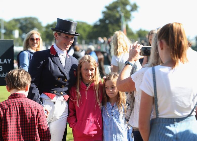 An adult wearing an equestrian uniform poses with children while an adult takes their picture.