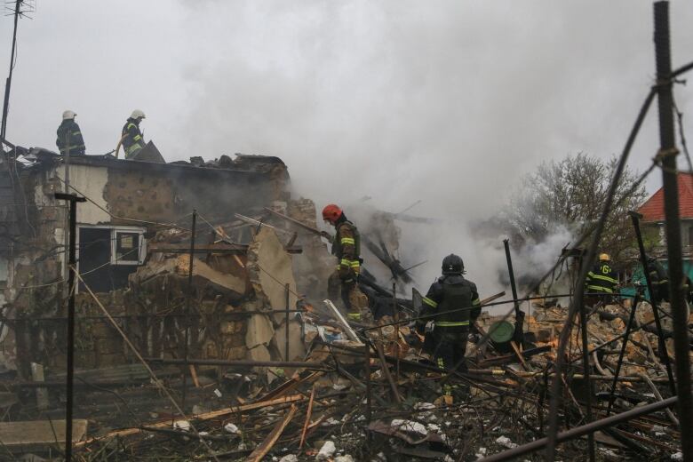 Firefighters stand atop and around a smoldering and destroyed building.