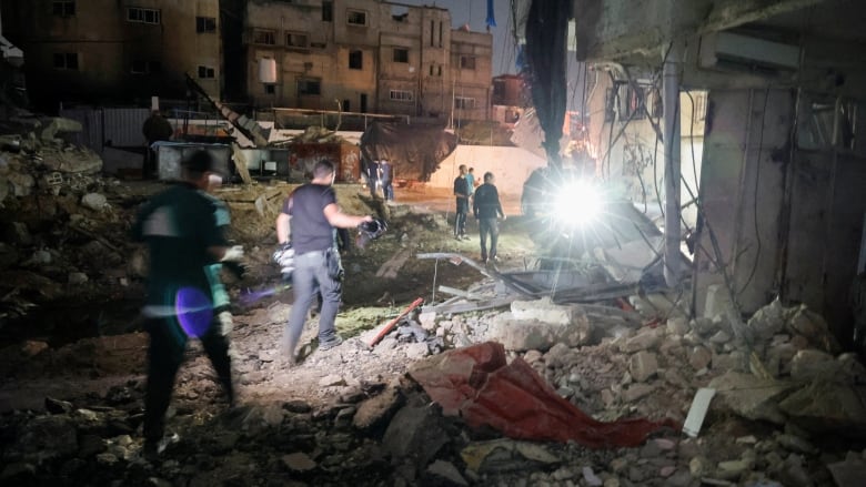 People walk amid the rubble near a damaged building.