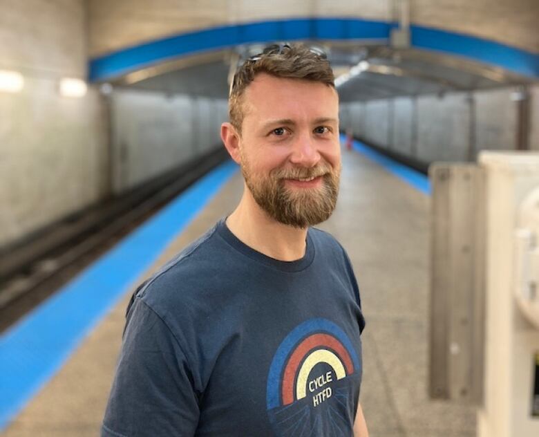 A man with a beard stands on an empty train platform