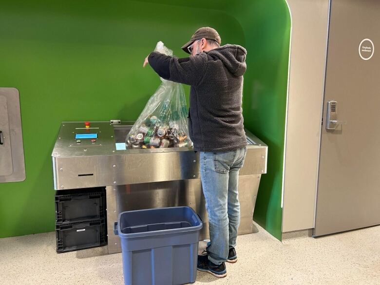 A man puts a bag of cans into a machine.