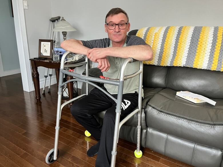 a man sits on his couch, leaning on a walker.