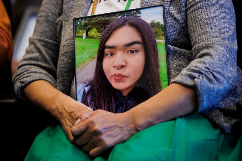 A close-up of a person's arms holding a framed photograph of a young teenager.