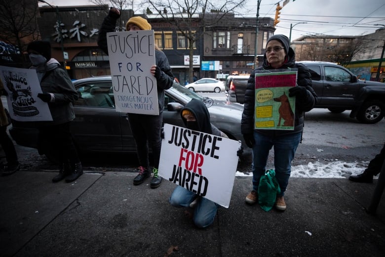 A group of people hold up signs reading 'Justice for Jared, Indigenous Lives Matter', and 'Stop using Dogs as Weapons'.