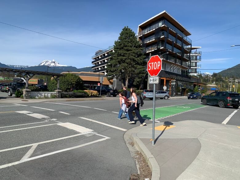 A pair of women cross a road in a city, with a mountain peak visible in the distance.