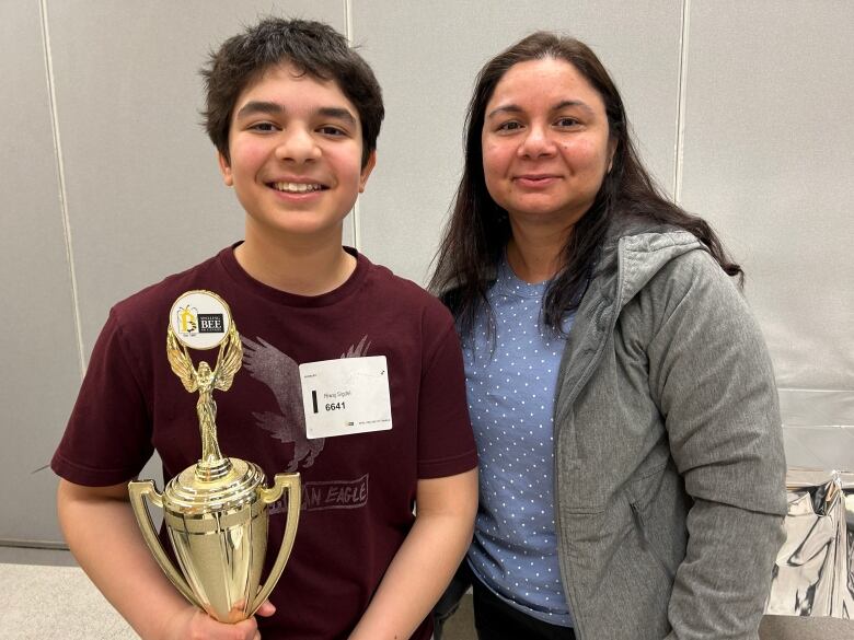 A boy holding a trophy standing next to a woman.