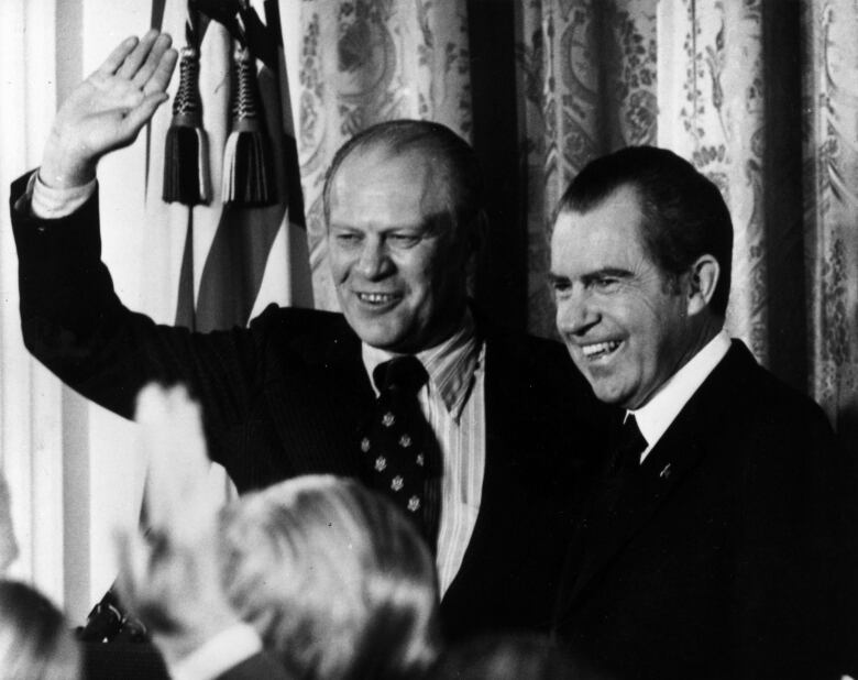 Two older cleanshaven men, each wearing suit and tie, are shown smiling in an old black and white photograph.