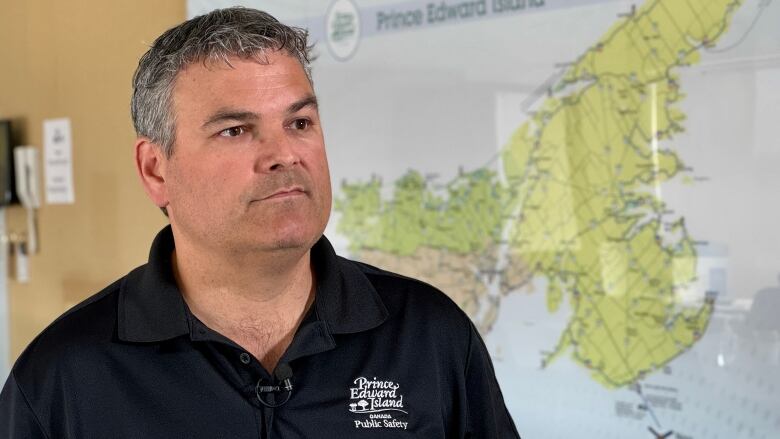 Man in black golf shirt with Prince Edward Island logo stands in front of a P.E.I. map on an office wall. 