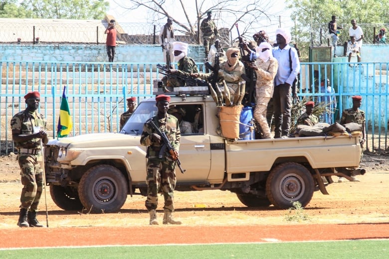 Rebel soldiers stand on and around a military truck.