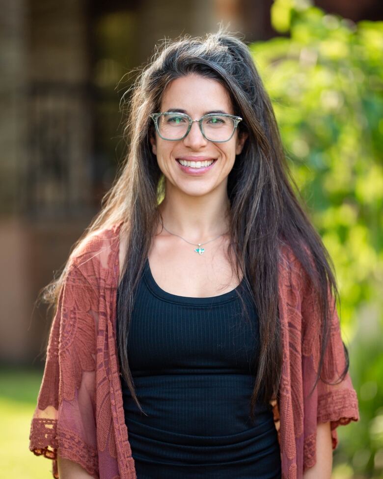 A smiling woman with glasses and long brown hair stands in front of a green background.