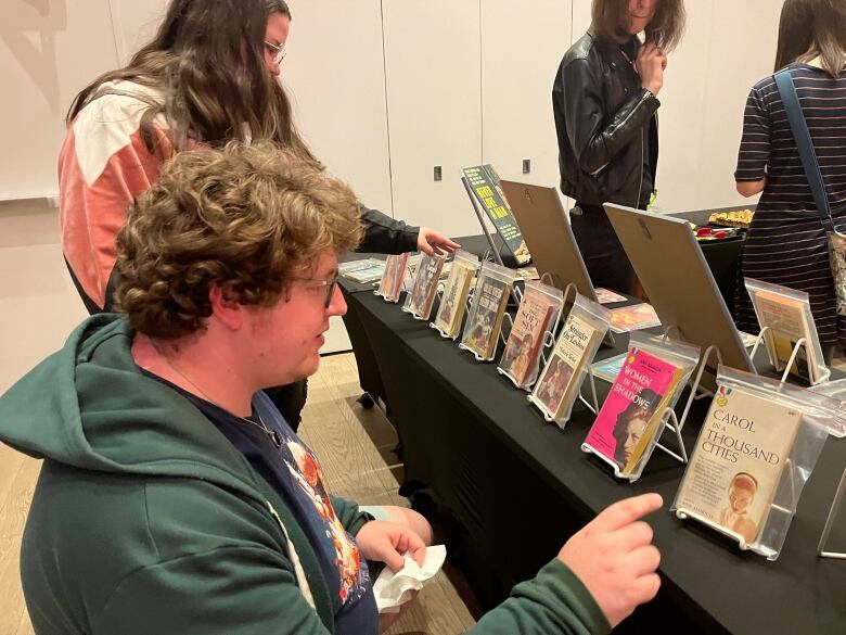 Two people are closely examining a book full of pulp fiction novels protected in plastic coverings on a black table. 