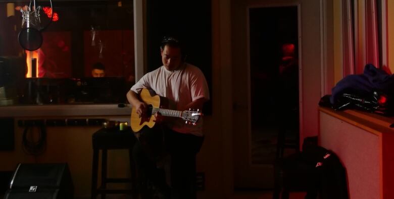 A guitarist plays in shadows in a darkened room.