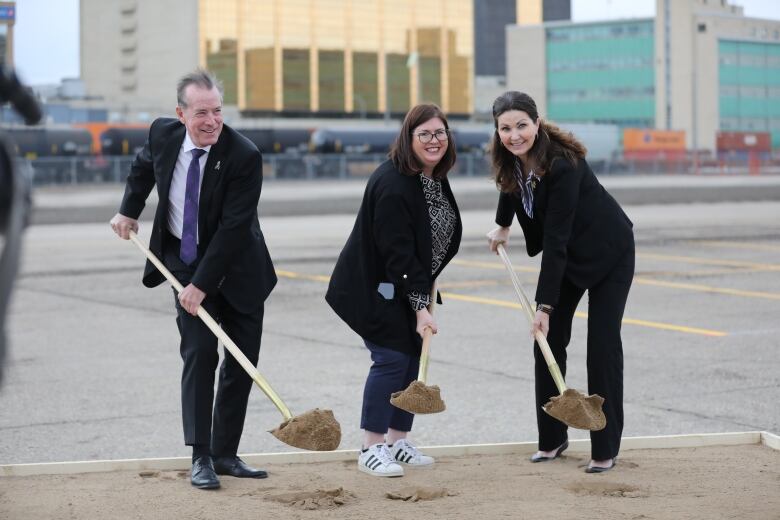 Three people, one man and two women, hold shovels full of dirt while posing for a photo.