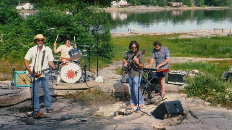 A rock band performs by a lake.