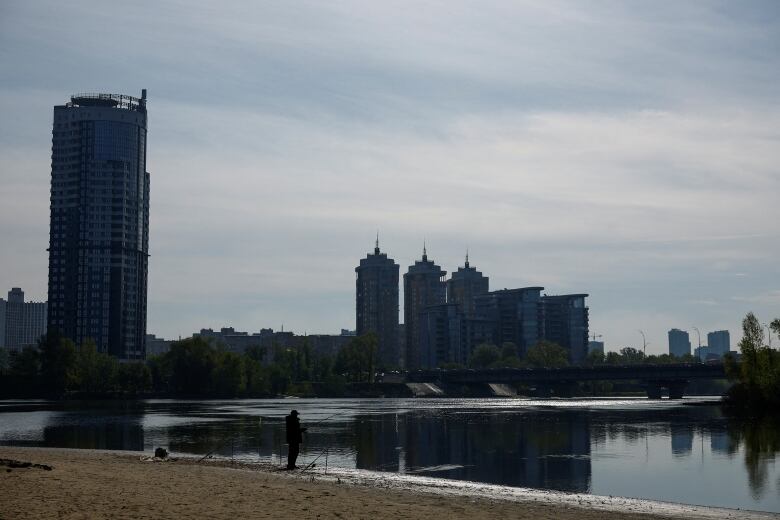 A man is seen holding a fishing rod on a beach in Kyiv.