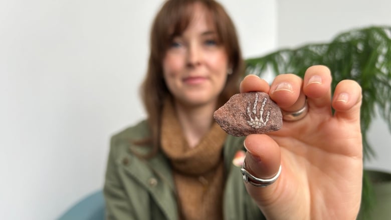 A woman holds a small sandstone rock with a fossil that looks like a tiny foot. 