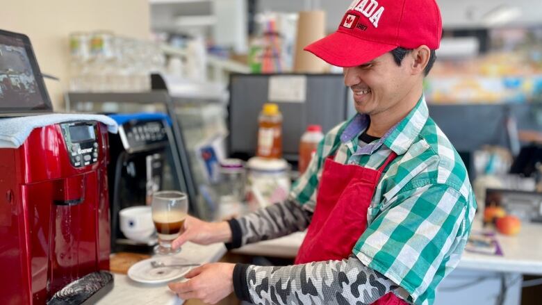 A man in an apron and ball cap prepares a Vietnamese coffee at a restaurant.