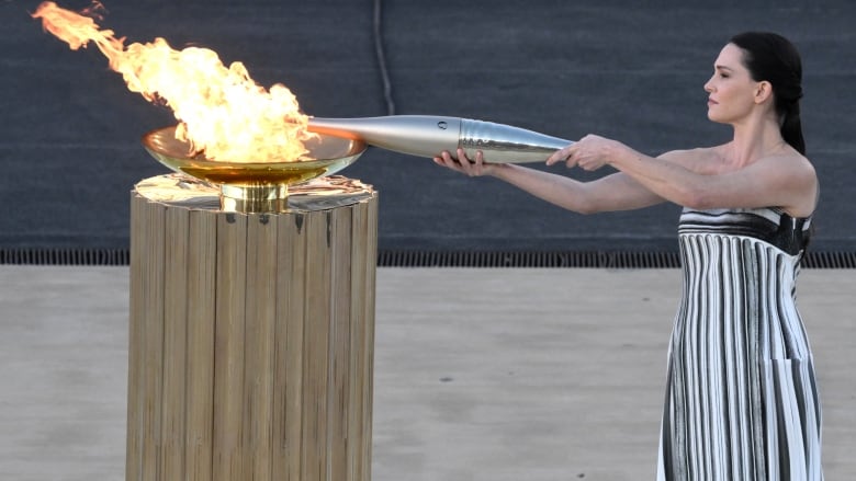 A woman lights a torch from a cauldron.