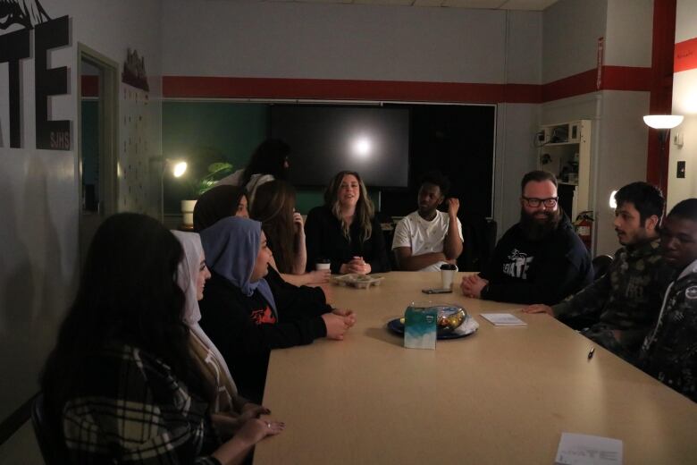 A group of youth and adults are pictured sitting around a table in a dimly lit room.