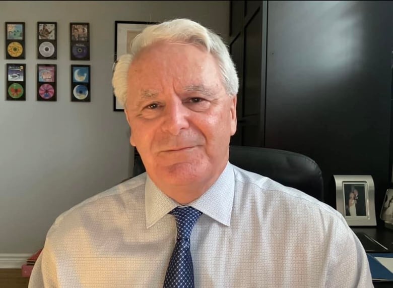 Man in a white collared shirt and blue tie looks at the camera