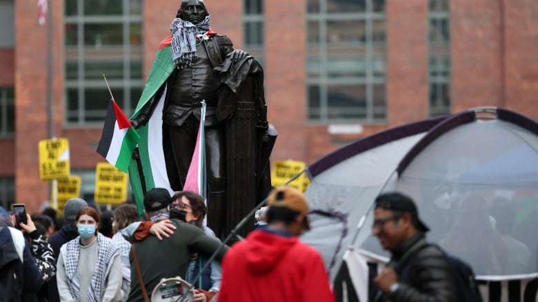 A statue of George Washington adorned with Palestinian flags and a keffiyeh, amid tents as students set up a protest encampment