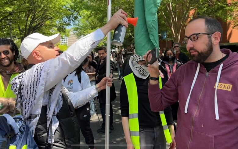 Man on left holds up air horn. Man on right records with phone