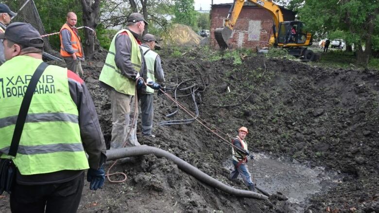 Utility workers operate next to a crater caused by a missile strike in Ukraine.