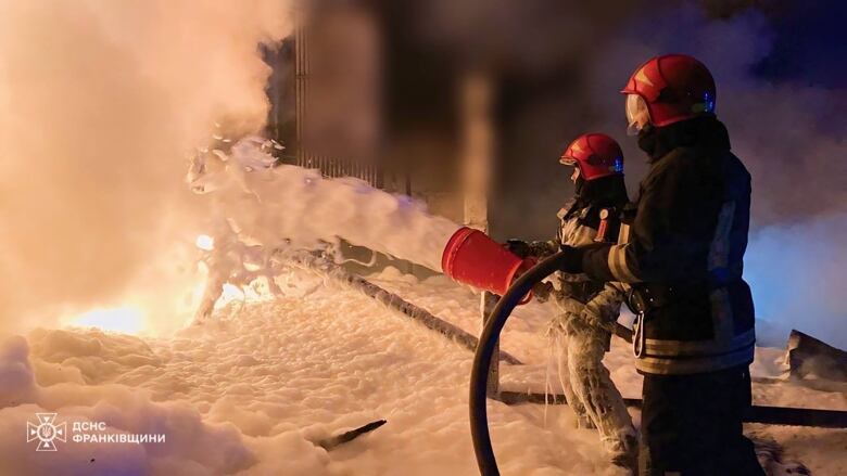 Two firefighters spray foam on a fire.