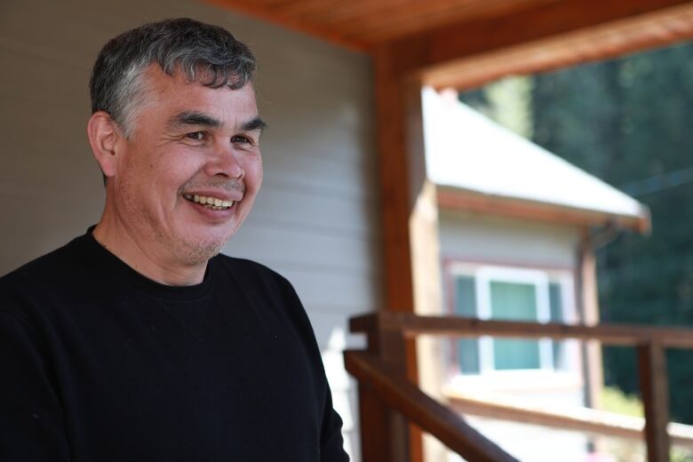 An Indigenous man smiles while talking in front of a white building.