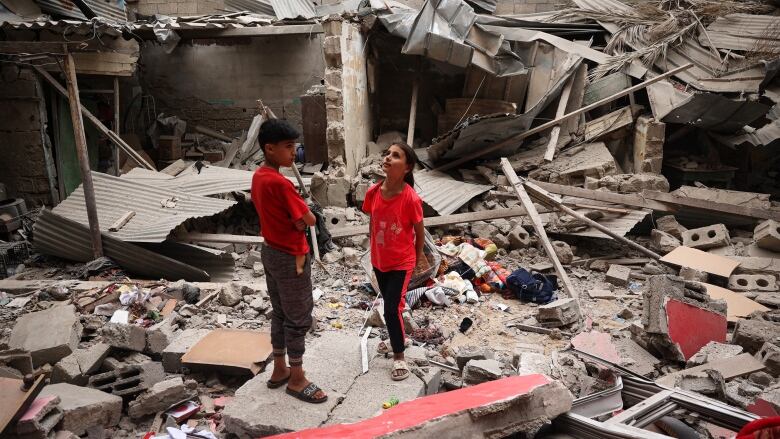 Two children stand amid the debris of a destroyed building.