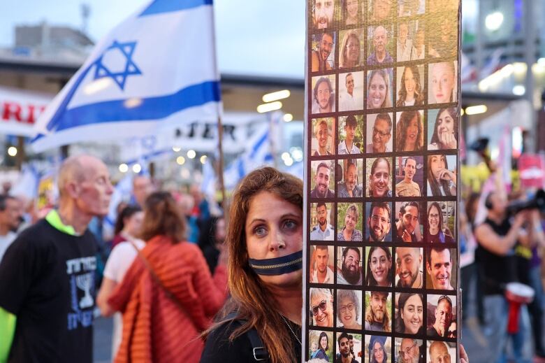 A protester with a zipper over their mouth holds a placard showing pictures of Israeli hostages.