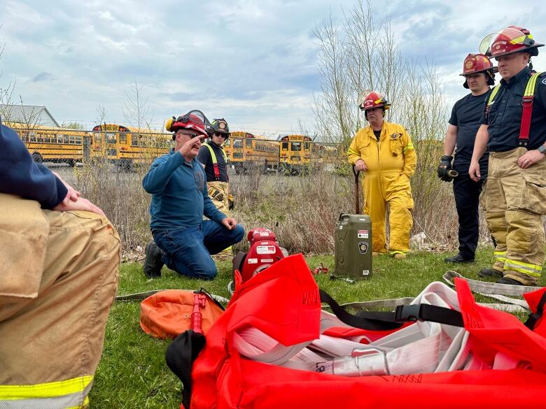 A group of fire fighters gather around an instructor during training. 