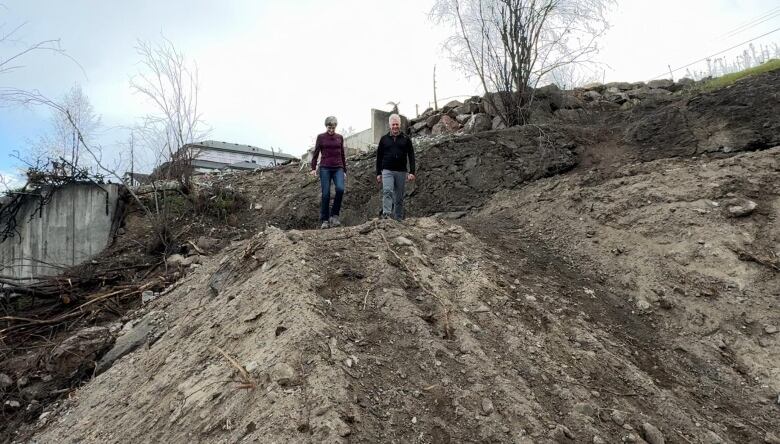 Two people walk among ashes and rubble