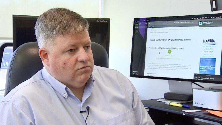 A man wearing a blue collared skirt sits in front of a computer screen.