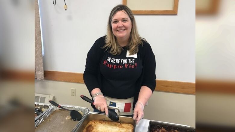 A woman wearing a black sweater with the words 'I'm here for the rappie pie!' is shown in front of a rappie pie.