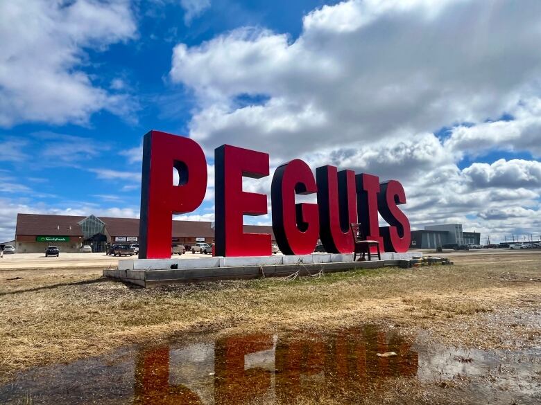 The red Peguis sign in front of the Peguis band office, reflected in a puddle.