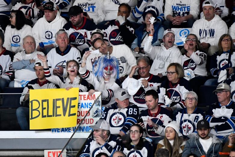 Winnipeg Jets fans wearing white in the stands, with one fan holding a sign that says, 'Believe.'