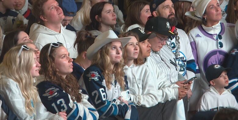 A crowd of people stare blankly up at a screen that is not in view.