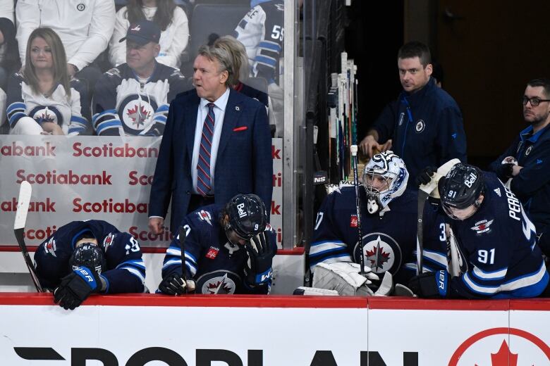 Hockey players in blue sit on a bench, some hanging their heads