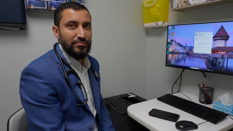 A man with a stethoscope hanging over his shoulders looks at the camera. 