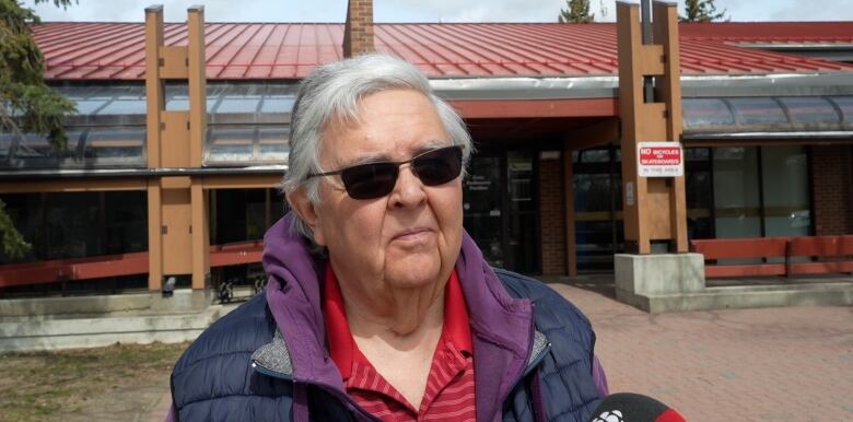 A 73-year-old man stands outside wearing sunglasses. 