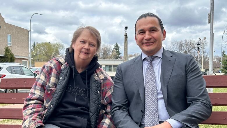 Two people sit side-by-side on a bench outside.