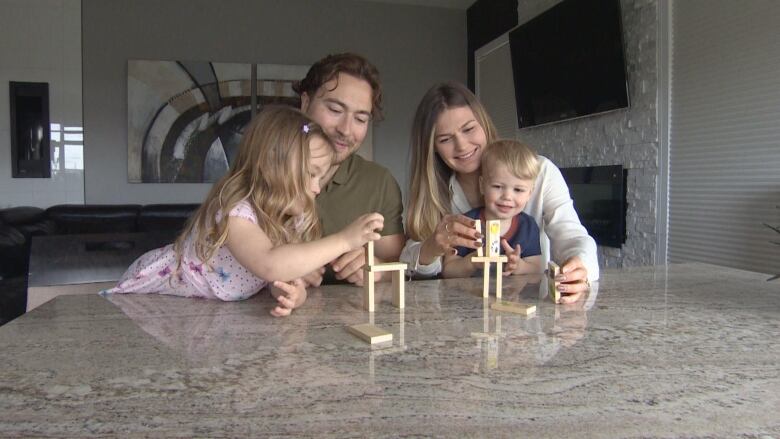 A man in a green shirt, woman in a white shirt and their two kids playing at the table