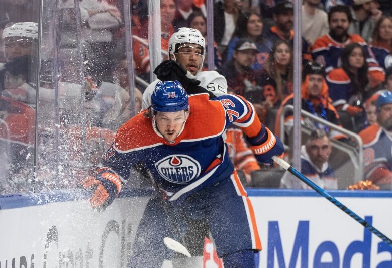 Two hockey players involved in a body check, lots of ice spray in the air. 