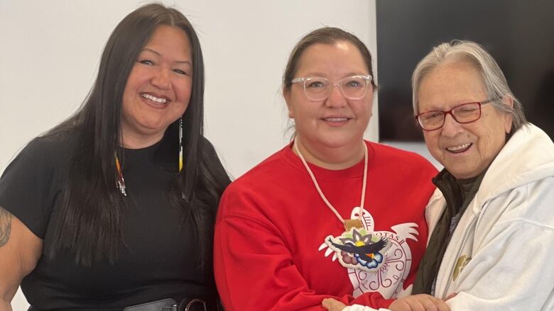 Three women stand together smiling with their arms around each other.