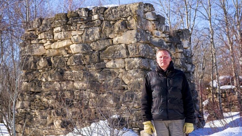 A man with short hair stands next to a stone structure outdoors in the winter.