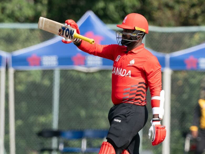 A man wearing a red uniform and a helmet holds up a cricket bat.