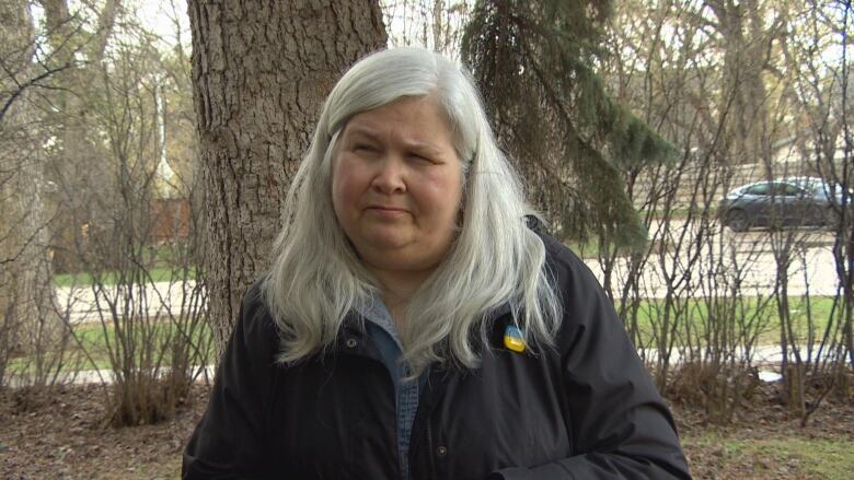 A woman stands in front of trees. 